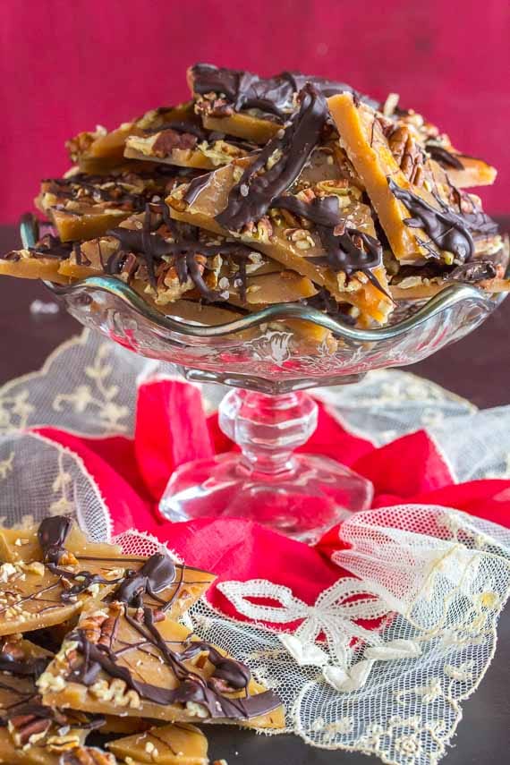 vertical image of pecan toffee image in footed glass dish with a red lace hankie