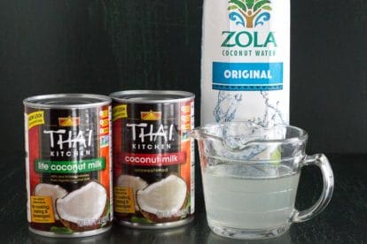 canned coconut milk and carton of coconut water against a dark background