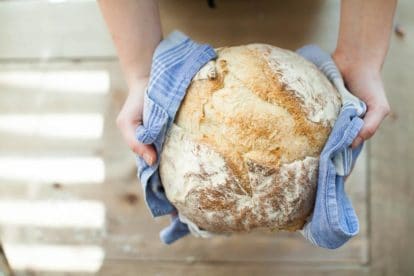 sourdough bread held in hands with a blue kitchen towel