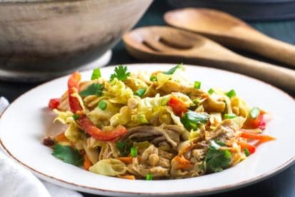 Low FODMAP Asian Chicken Salad on a white plate with wooden bowl and serving implements in background