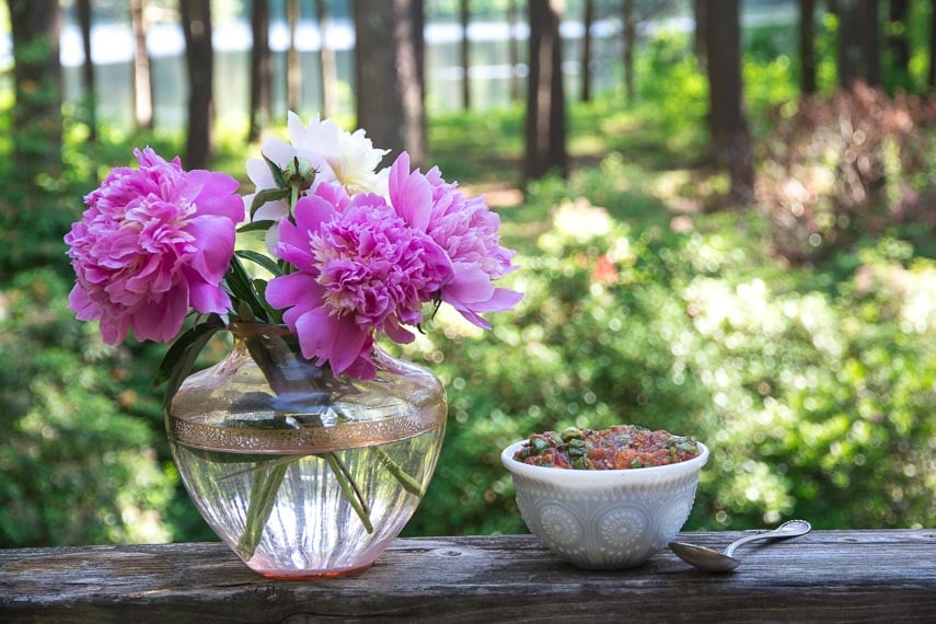 white bowl of grilled salsa alongside pink glass vase of peonies