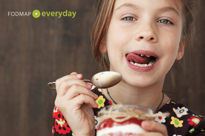 young girl eating yogurt parfait with spoon and licking her lips