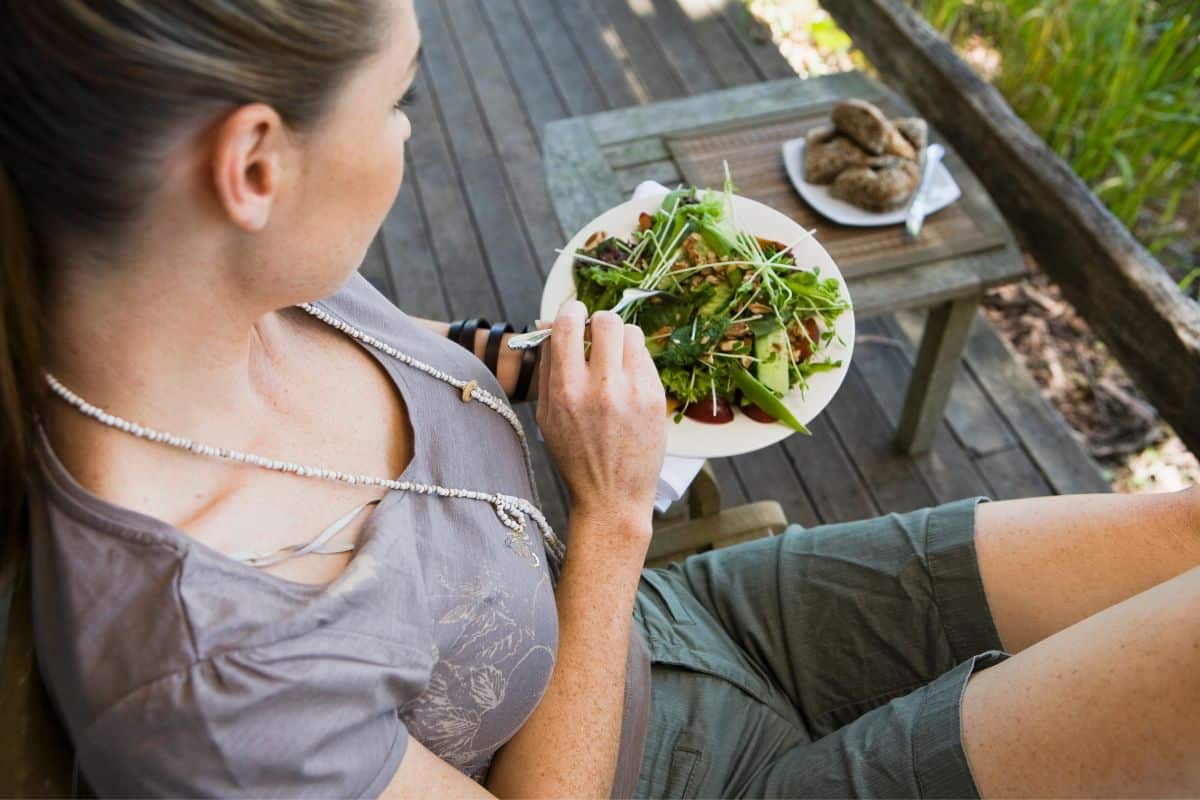 Young woman sitting on a deck outside eating a salad