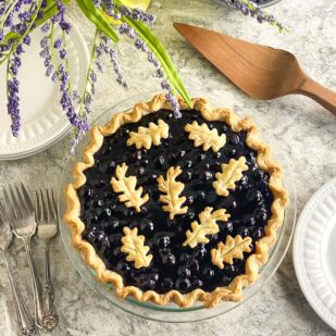 horizontal image overhead of low FODMAP Fresh Blueberry Pie on gray quartz with white plates, silver forks