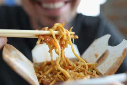 Smiling man eating spicy noodle chinese food with vegetable using chopsticks