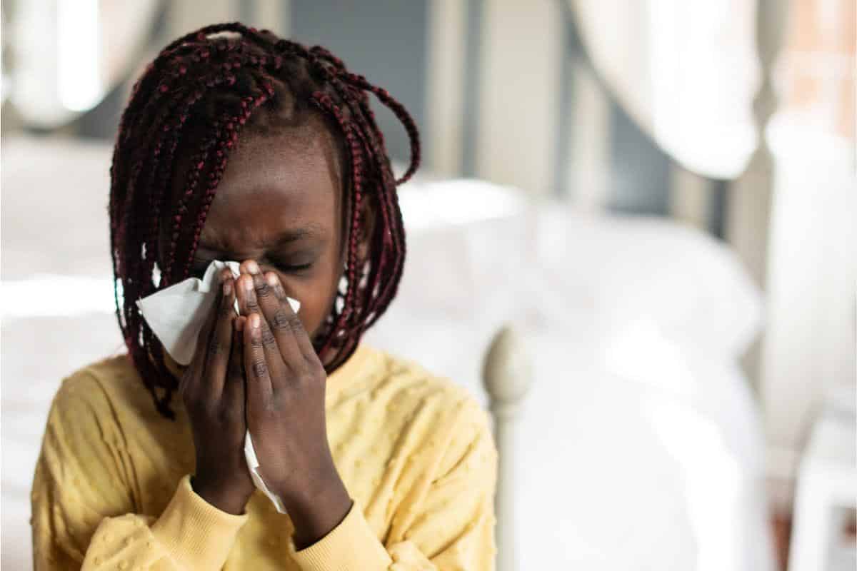 young girl sneezing into tissue.