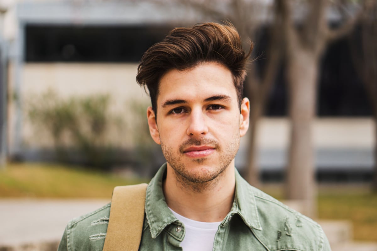 Portrait of teenage male student looking serious at camera in a college. Caucasian guy standing in university campus.