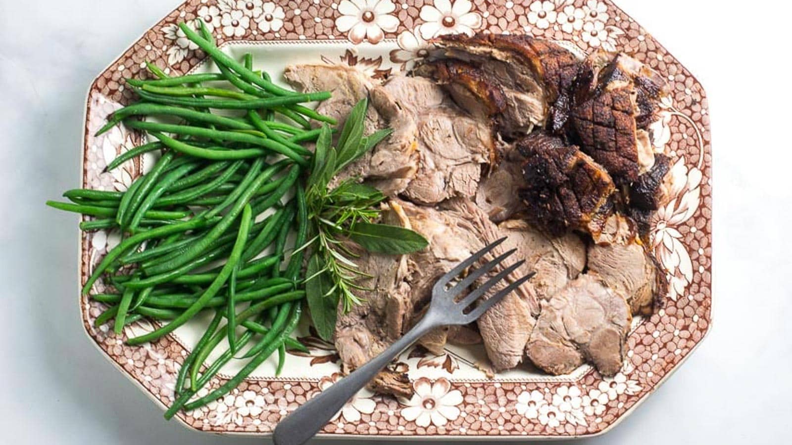 Porchetta-Pork-Roast-sliced-with-green-beans-on-a-brown-and-white-platter-with-meat-fork.