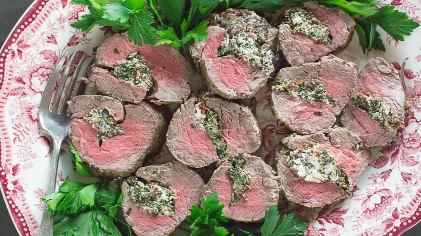 Overhead-image-of-Beef-Tenderloin-Stuffed-with-Goat-Cheese-Spinach-Sun-Dried-Tomatoes-on-a-red-and-white-platter.