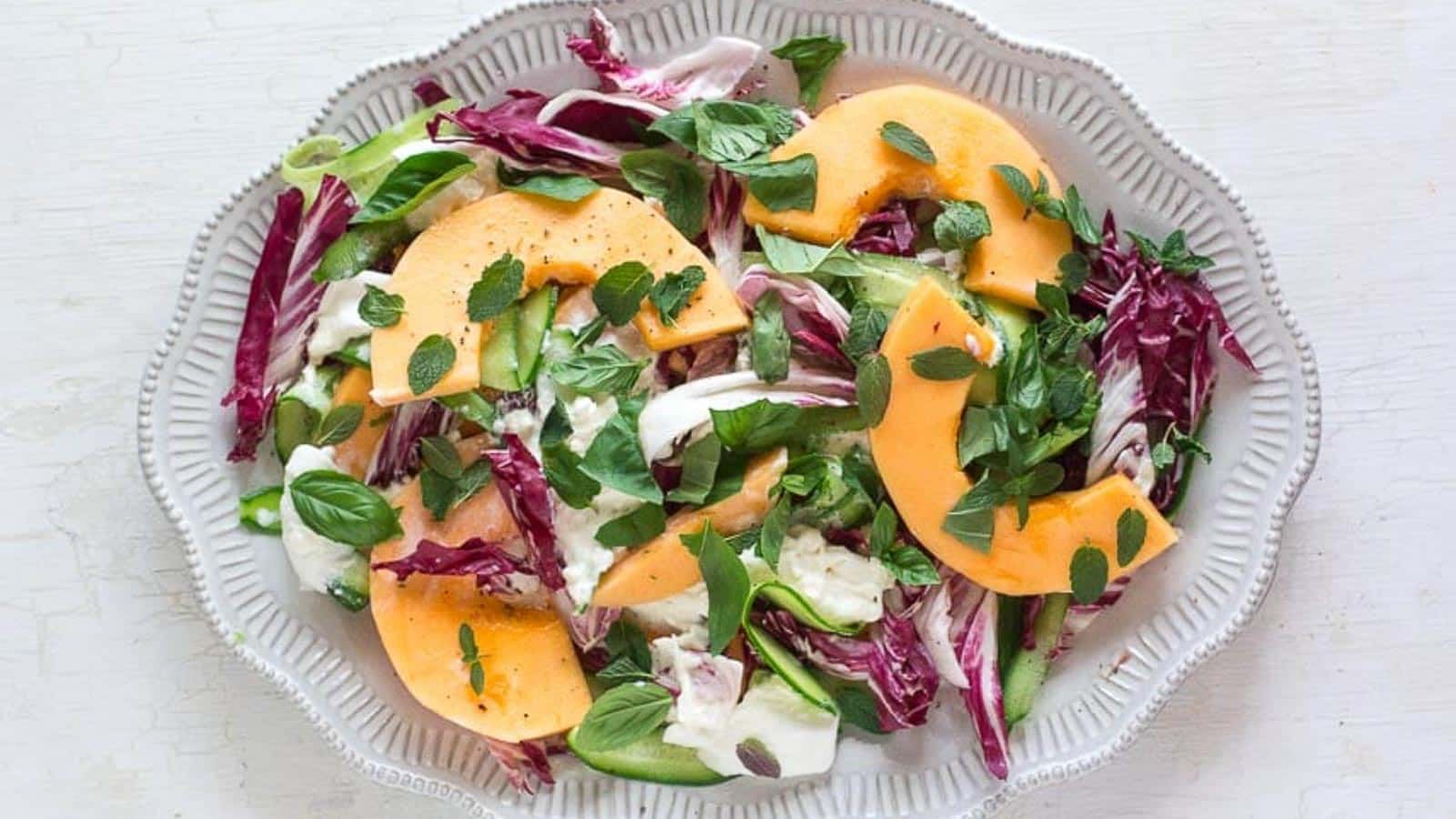 cantaloupe-cucumber-and-burrata-salad-with-herbs-on-a-white-platter-and-white-wooden-surface.