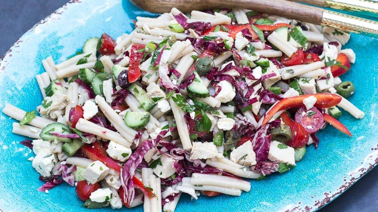 Mediterranean-Pasta-Salad-on-oval-aqua-platter-with-wooden-serving-spoons.