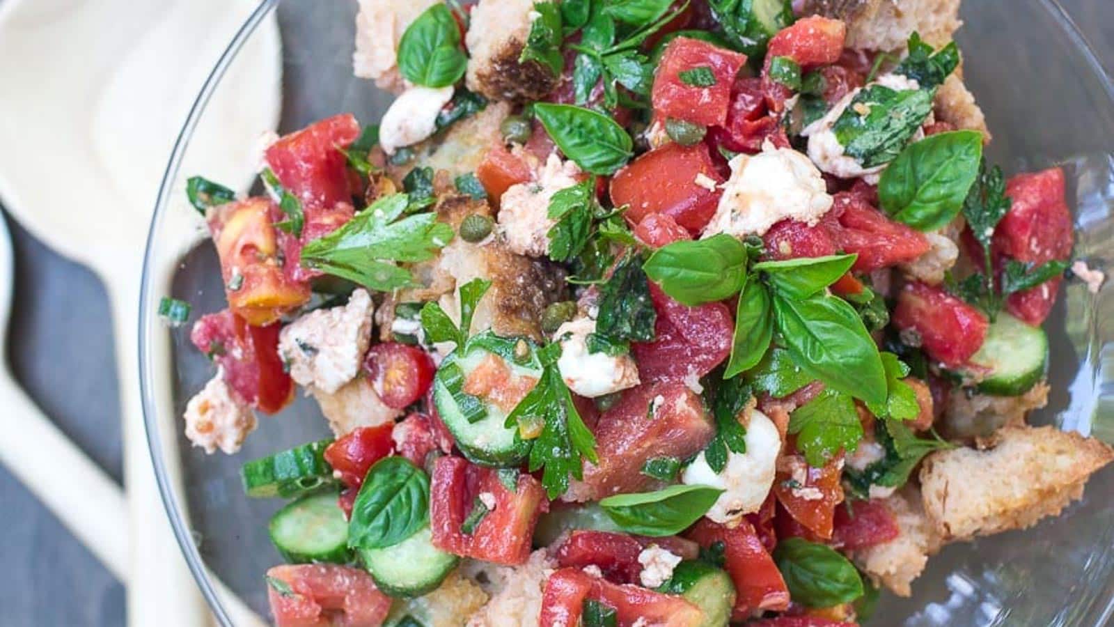 Panzanella-with-Tomatoes-Cucumbers-basil-in-a-glass-pedestal-dish-with-wooden-servers-alongside.