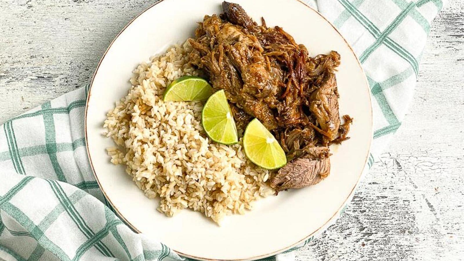 Instant-Pot-Cuban-Style-Pork-on-white-plate-with-brown-rice-and-limes-white-painted-wood-background.