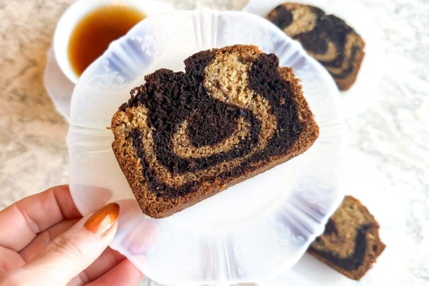 Low FODMAP Marbled Banana Bread on plate held in hand, tea in background.