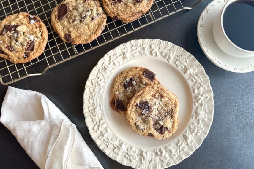 Low FODMAP Tahini Chocolate Chunk Cookies on white plate and rack. Cup of coffee.