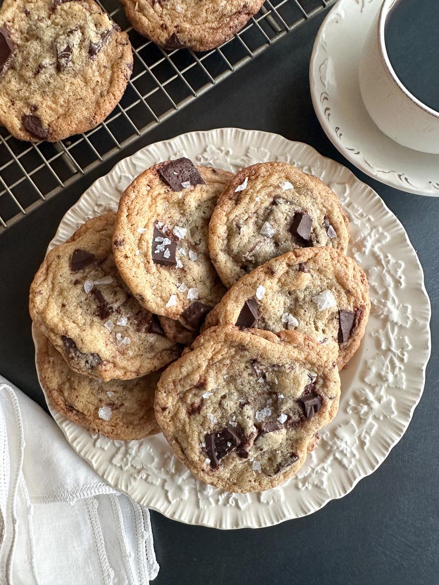 Low FODMAP Tahini Chocolate Chunk Cookies on white plate and rack. Cup of coffee. Closeup.