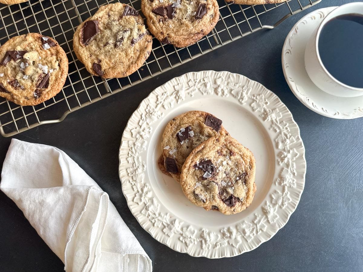 Low FODMAP Tahini Chocolate Chunk Cookies on white plate and rack. Cup of coffee.